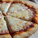 King arthur gluten free pizza crust - the image shows a freshly baked pizza on a wooden cutting board. the pizza has a golden brown crust and is topped with melted cheese and tomato sauce. the cheese is white and bubbly, and the tomato sauce is a deep red color. there are six slices of the pizza arranged in a diagonal line on the cutting board, with the top slice slightly overlapping the bottom one. the background is blurred, but it appears to be a kitchen countertop with a gray cloth napkin.
