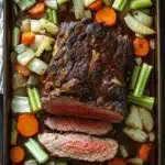 Roast beef marinade slow cooker - the image shows a rectangular baking dish filled with a roast beef dish. the roast beef is cooked medium-rare and has a rich, dark brown color. it is garnished with sliced carrots, celery, and onions. the dish is sitting on a wooden table with a gray and white striped napkin on the side. the vegetables are arranged in a way that they are overlapping each other, creating a colorful and appetizing presentation.