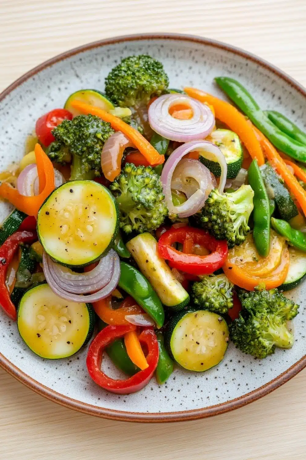 Sauteed vegetables in sauce - the image is a close-up of a colorful salad in a bowl. the salad is made up of various vegetables, including broccoli, red bell peppers, sliced cucumbers, and red onions. the vegetables are arranged in a circular pattern on a white plate with a speckled pattern. the colors of the vegetables are vibrant and the dish looks fresh and appetizing. the bowl is sitting on a wooden table.