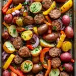 Sheet pan sausage and potatoes dinner - the image shows a baking tray filled with a variety of vegetables. the tray is lined with parchment paper and is placed on a wooden table. the vegetables include red potatoes, yellow bell peppers, red onions, and green onions. there are also some herbs sprinkled on top, likely parsley or cilantro. the dish appears to be freshly cooked and ready to be served.