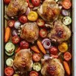 Sheet pan vegetables with chicken - the image shows a rectangular baking tray with six pieces of chicken on it. the chicken is cooked to a golden brown color and appears to be seasoned with herbs and spices. the tray is filled with sliced tomatoes, onions, and carrots, which are arranged in a circular pattern around the chicken. the tomatoes are bright red and appear to be ripe and juicy, while the onions are sliced into thin strips. the carrots are orange and are cut into small pieces. the vegetables are also sliced and arranged around the tray, adding a pop of color to the dish. the background is a white marble countertop.