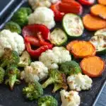 Vegetables in air fryer oven - the image shows a black rectangular baking tray filled with various types of vegetables. on the left side of the tray, there are roasted cauliflower, broccoli, red bell peppers, and sliced carrots. the vegetables are arranged in a way that they are overlapping each other, creating a colorful and appetizing display. the tray appears to be made of a dark-colored material, possibly parchment paper or parchment paper. the background is blurred, but it seems to be a kitchen countertop.