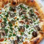 White sauce truffle pizza - the image is of a freshly baked pizza on a wooden cutting board. the pizza has a golden brown crust and is topped with melted white cheese and sliced mushrooms. the mushrooms are arranged in a circular pattern on top of the cheese. there are also a few sprigs of fresh parsley scattered around the cutting board, adding a pop of green color to the dish. the background is a white marble countertop.