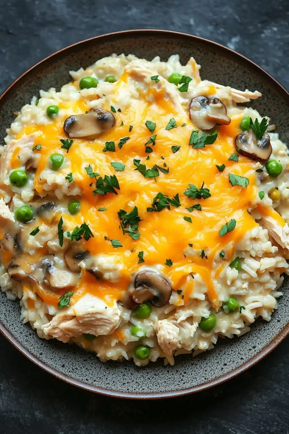 Chicken rice casserole crockpot - the image is a close-up of a plate of risotto with chicken and mushrooms. the risotto is white and fluffy, and the chicken is cooked to a golden brown color. the mushrooms are sliced and arranged on top of the risotto, and there are small green peas scattered throughout. the dish is garnished with a sprig of parsley. the plate is brown and has a textured surface. the background is a dark grey countertop.