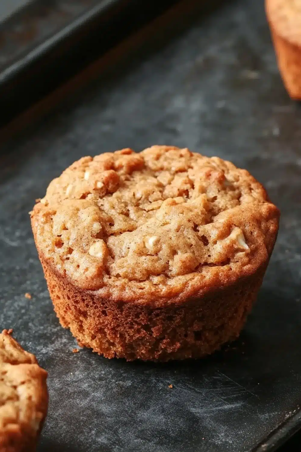 High protein vegan breakfast muffin - the image shows a freshly baked muffin on a black baking tray. the muffin is round and golden brown in color, with a crumbly texture on top. it appears to be freshly baked and has a soft, fluffy interior. the tray is lined with parchment paper, and there are a few more muffins visible in the background. the overall mood of the image is warm and inviting.