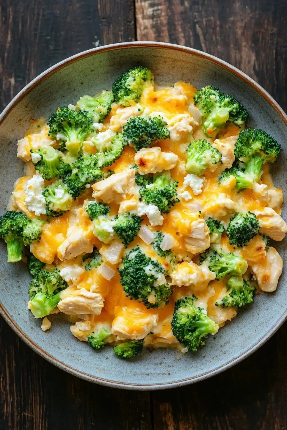 Macro chicken broccoli casserole - the image is a close-up of a bowl of food. the bowl is made of ceramic and is placed on a wooden table. the food appears to be a casserole dish with broccoli and chicken mixed in. the broccoli is bright green and looks fresh and healthy. the chicken is cut into small pieces and is covered in melted cheese. the cheese is a creamy yellow color and is scattered throughout the dish. the dish looks like it is ready to be eaten.