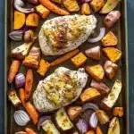 Roasted chicken breast and root vegetables - the image shows a baking tray with two pieces of chicken and roasted vegetables. the chicken is golden brown and appears to be seasoned with herbs and spices. the vegetables are cut into small cubes and are arranged around the chicken. there are also some red onions and carrots scattered throughout the tray. the tray is lined with parchment paper and is placed on a dark grey countertop.